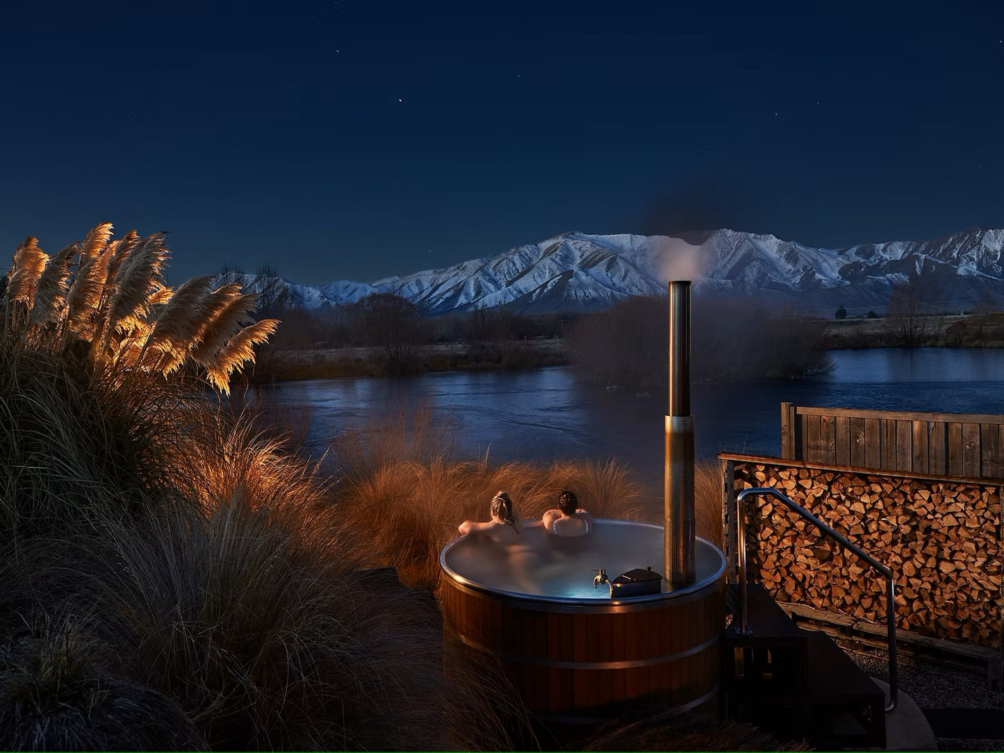relaxing in outdoor wood-fired hot tub at night with mountain view and lake 