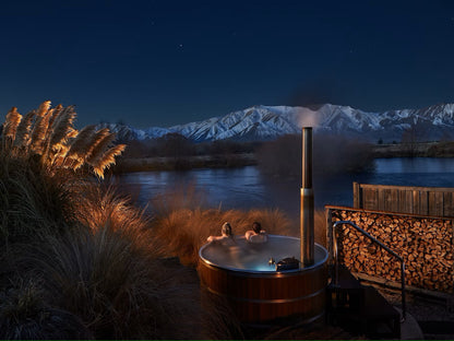 relaxing in outdoor wood-fired hot tub at night with mountain view and lake 